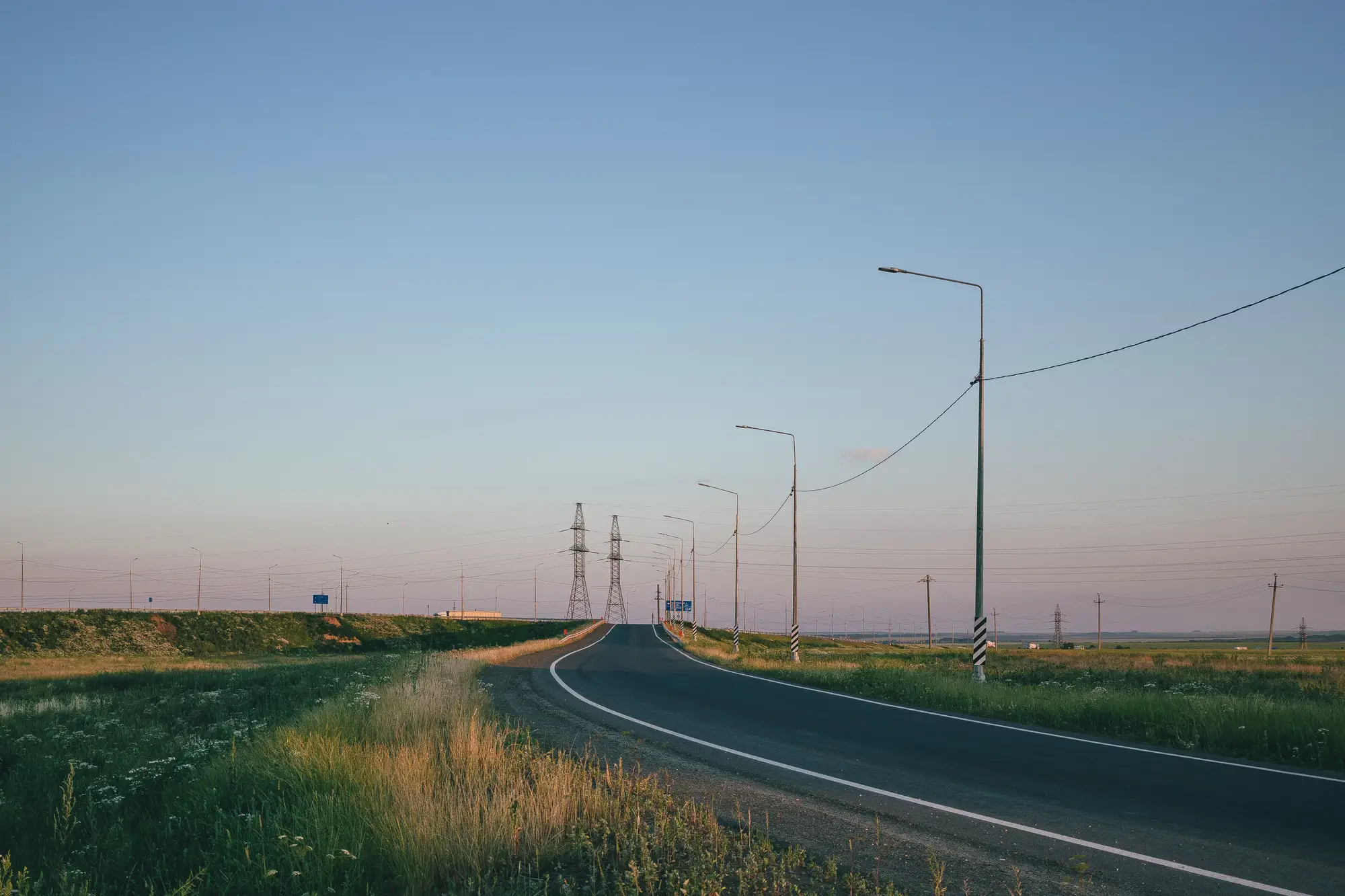An empty two-lane road running through open country at dusk, power lines along one side
